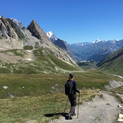 Wanderin mit Rucksack und Stöcken blickt über ein Alpental.
